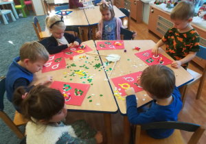 Dzieci przy stoliku ozdabiają wzór materiałem plastycznym o różnej fakturze.